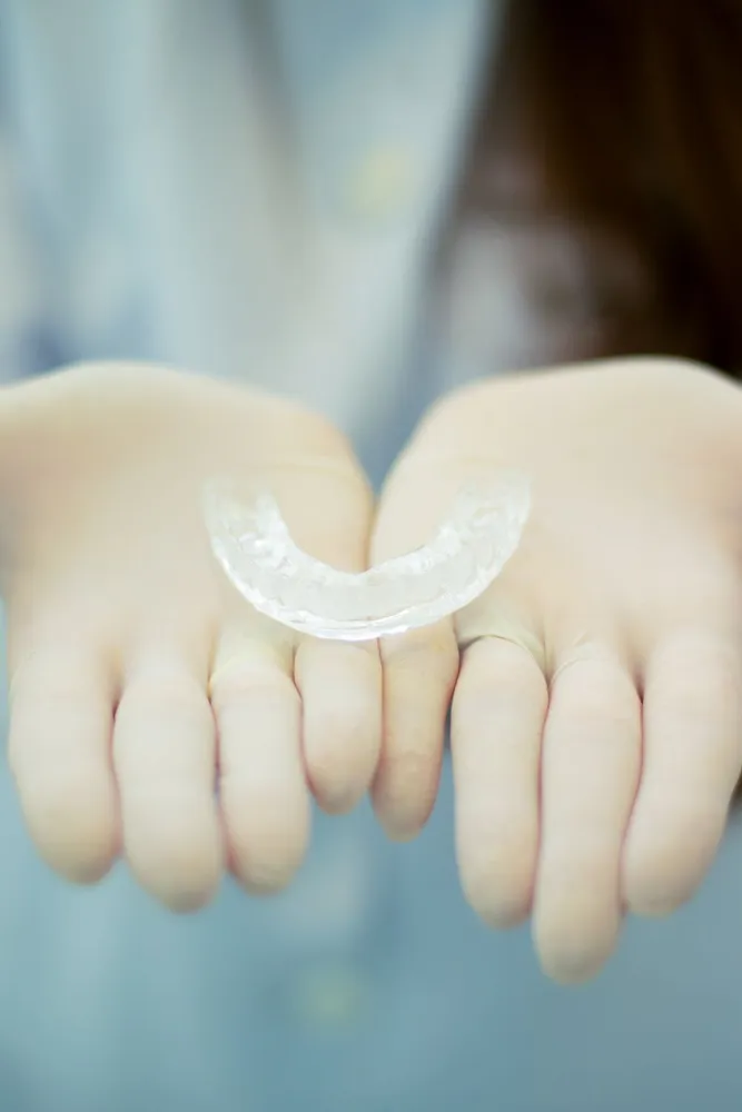 A clinician holding a clear dental aligner — the type used for Invisalign treatment at Pearly White Dentistry.