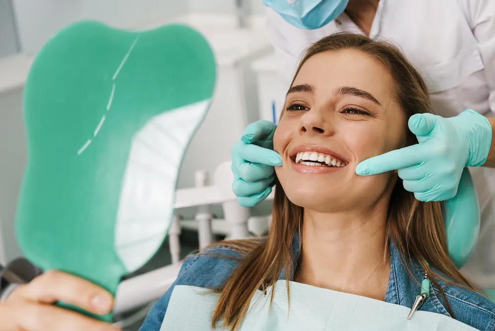 A patient at Pearly White Dentistry holding a mirror to view her smile.